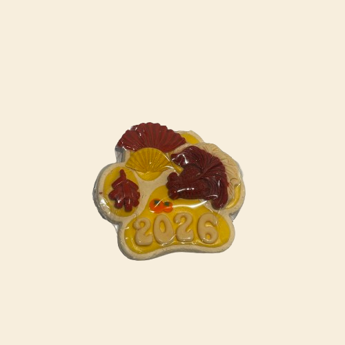 A handcrafted 2026 New Year celebration dog cookie featuring lucky koi fish and festive fan designs made from goat milk icing on a chicken breast base.