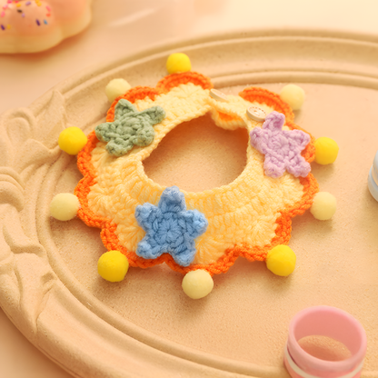 Close-up of the Dopamine Delight Collar. Hand-knitted from soft yellow milk cotton yarn with pastel stars and pom-poms for a sensory-soothing feel.