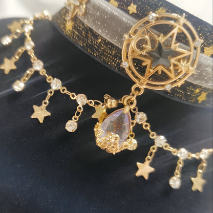 Detailed close-up of the Galaxy Sorceress Cat Collar. Showcases the magnificent gold star emblem, shimmering black-and-gold ribbon, and a draping iridescent teardrop rhinestone