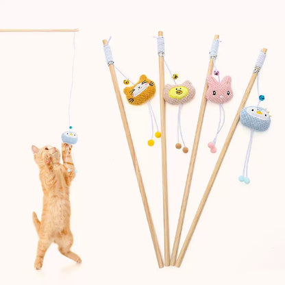 An orange tabby kitten leaps into the air to catch a blue penguin plush toy attached to a LéJoyee natural wood teaser wand, with four other cute plush wands standing vertically in the background.