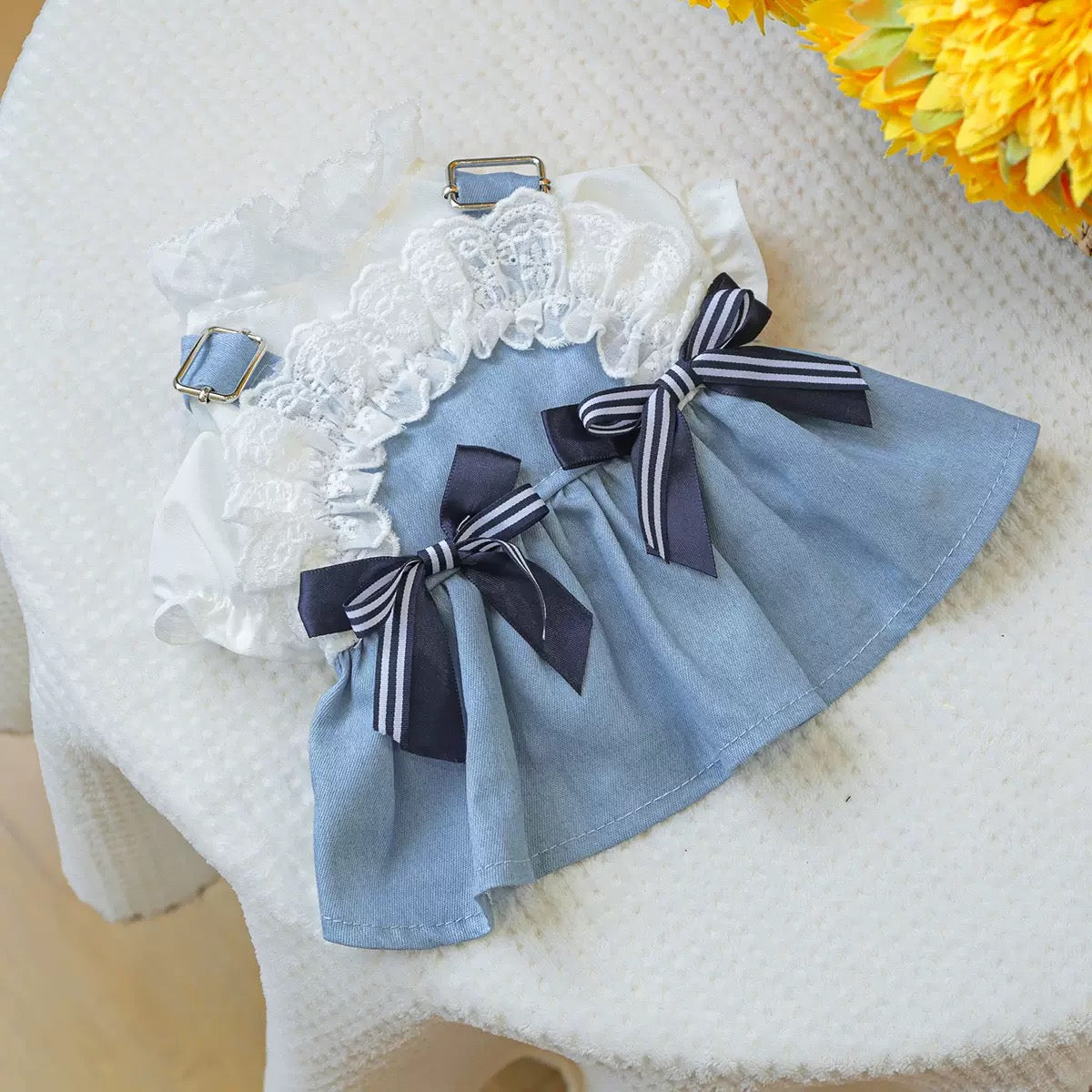 Flat lay of the Sea Breeze Denim Pinafore Dress for dogs. Features light-wash breathable denim, tiered white lace ruffles, and navy striped satin bows for a coastal vacation look.