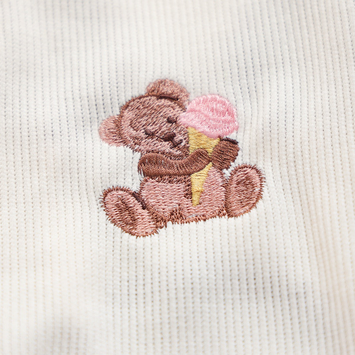 Macro shot of the tiny bear holding a pink ice cream cone embroidery. High-quality stitching that adds a dopamine design element to the white vest
