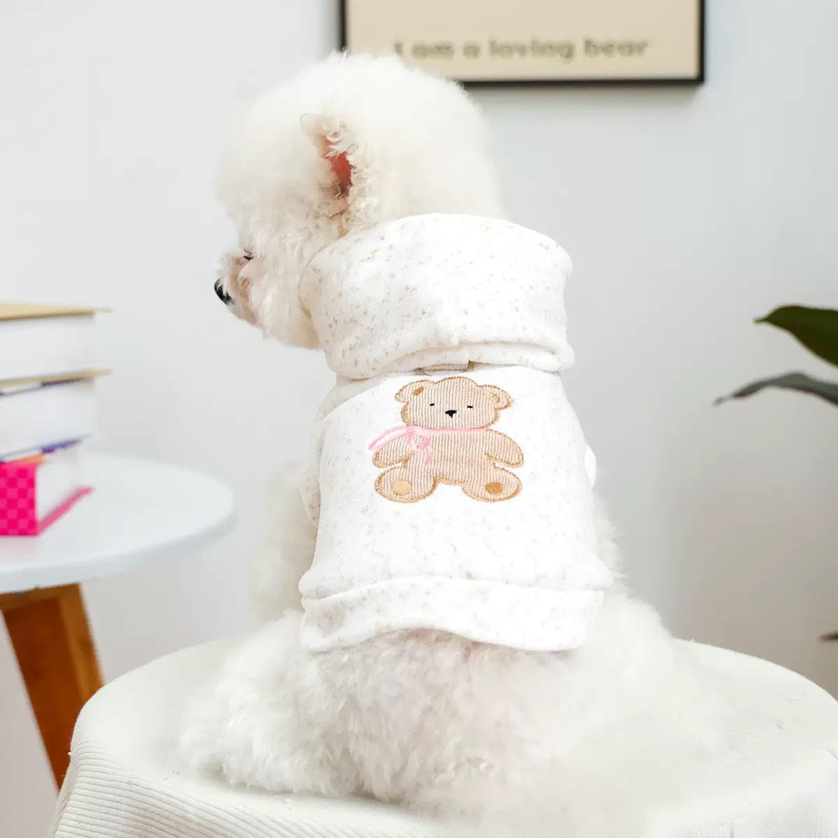 Back view of a white Bichon wearing the Teddy Hug Hoodie. Features a high-quality teddy bear embroidery with a pink bow on a cream speckled knit fabric