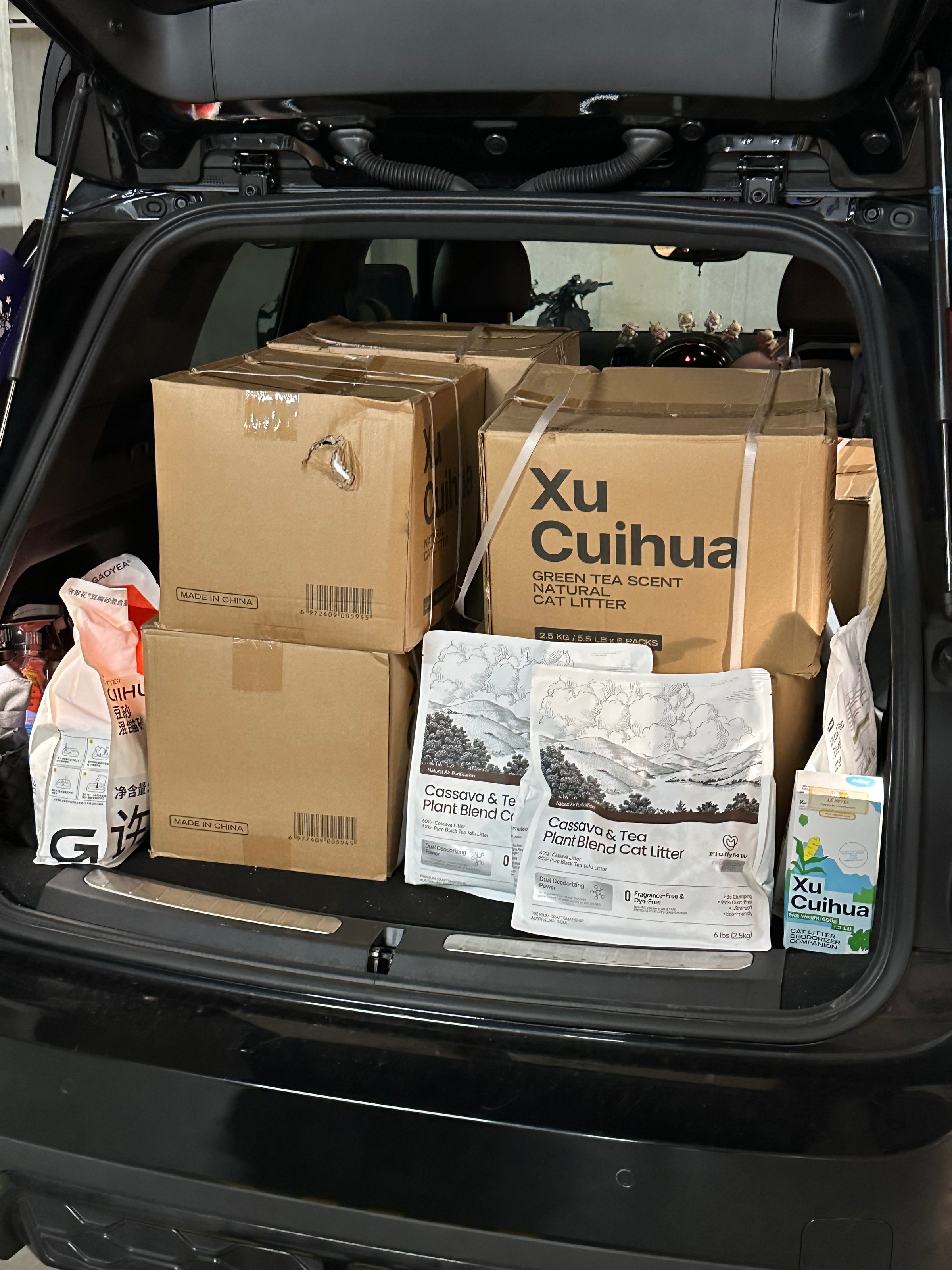 Trunk of a car filled with boxes and bags, including 'Xu Cuihua' cat litter packaging.