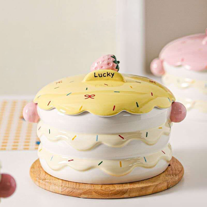 A whimsical strawberry cake ceramic pet bowl decorated with colorful sprinkles and a matching lid topped with a Lucky strawberry, placed elegantly on a round wooden coaster.