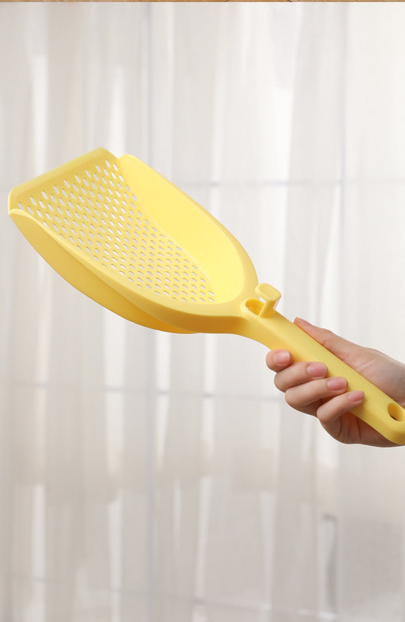 Close-up of a hand comfortably gripping the 34.5cm ergonomic handle of the yellow litter scoop, showing the clever built-in hanging clip mechanism.