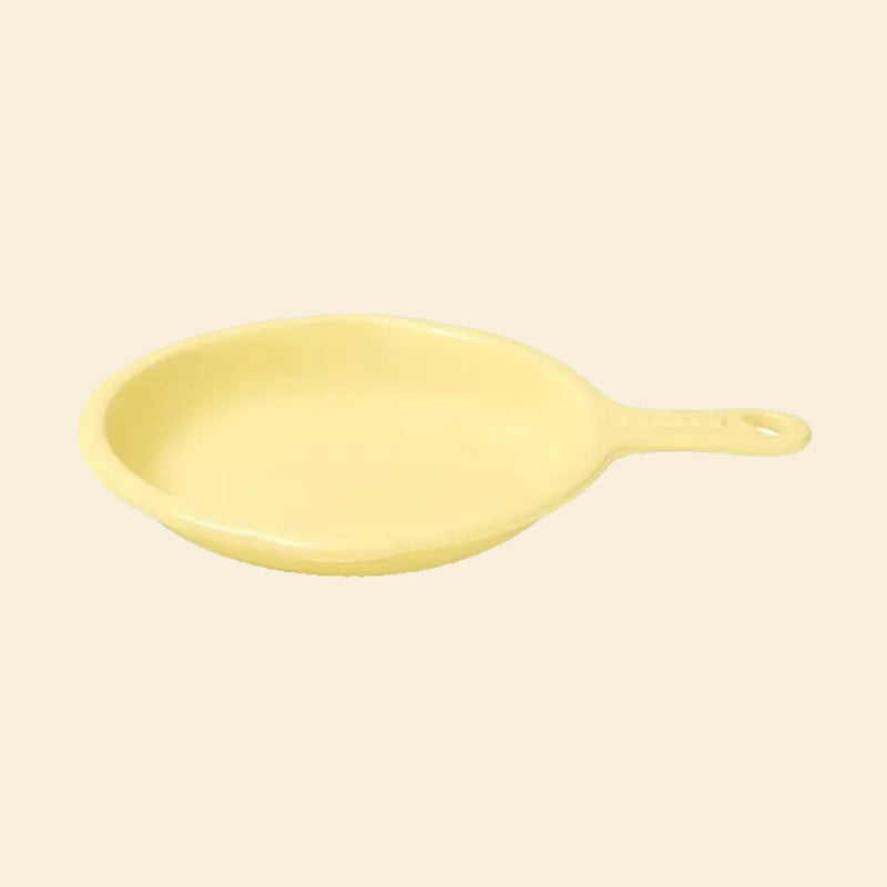 A clean, angled view of the Mango Little Skillet Ceramic Pet Plate in pastel yellow. Features a sturdy handle with a hanging hole for mess-free serving.