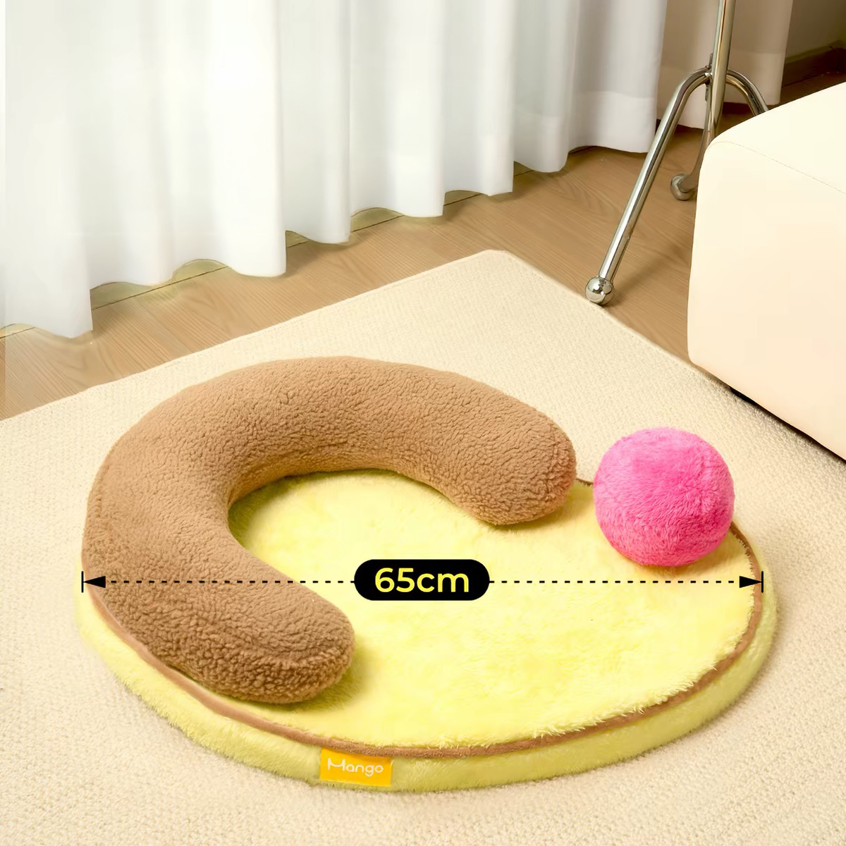 Size guide for the Mango Pet Bed showing a generous 65cm length. Featuring a brown U-shaped bolster pillow and a pink fluffy play ball on a yellow mat.