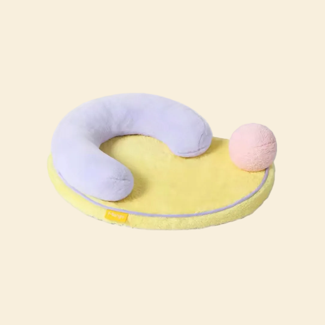 The Mango Pet Bed featuring a purple U-shaped security pillow, yellow base, and a detachable pink play ball, crafted from ultra-soft faux rabbit fleece.