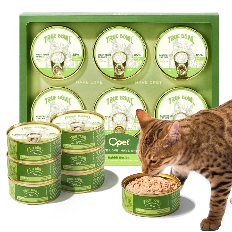Cat eating from a can of True Bowl pet food with multiple cans and packaging in the background.
