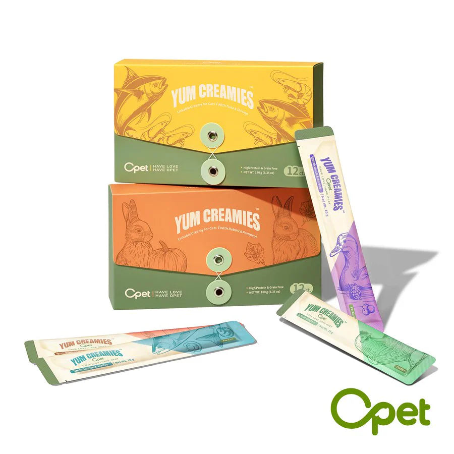 A display of OPET Yum Creamies lickable cat treats, showing the individual 15g squeeze tubes in various flavors like Chicken and Duck, alongside the Tuna and Rabbit flavor 12-pack boxes.