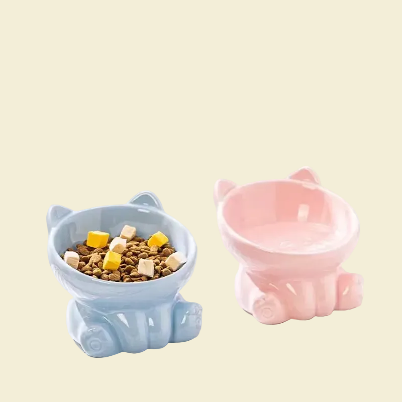 Two pastel-colored elevated ceramic cat bowls, one in light blue filled with kibble and freeze-dried treats, and the other in soft pink.
