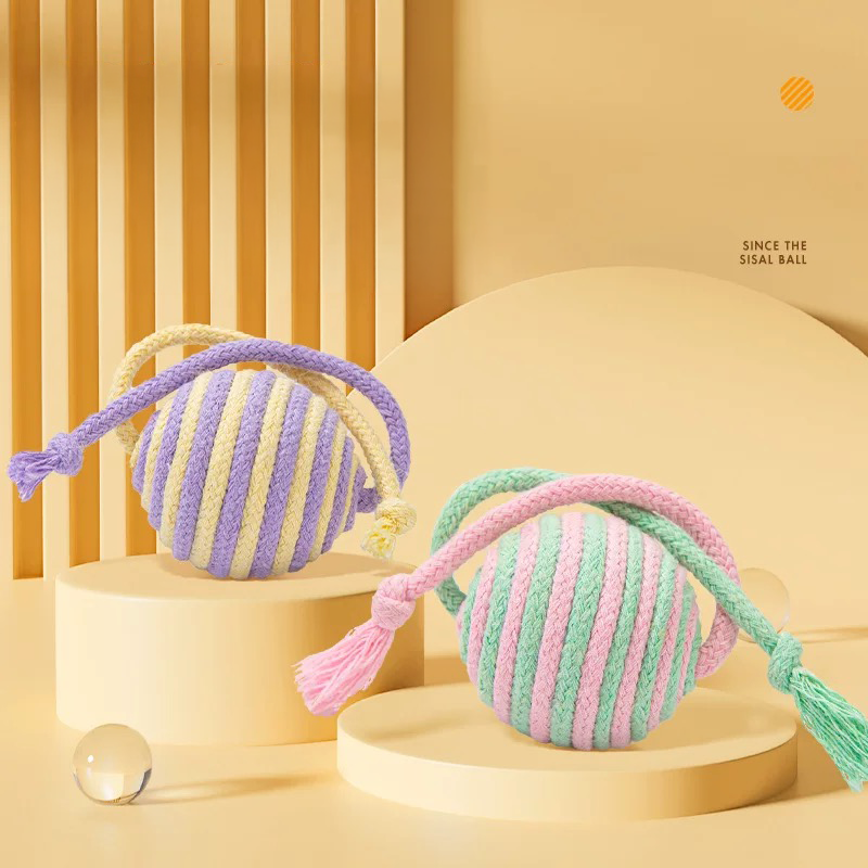 Two pastel striped sisal cat toy balls, one in purple and yellow, the other in pink and green, beautifully displayed on beige geometric podiums.