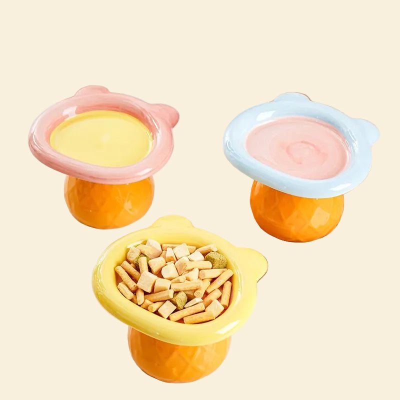 A vibrant collection of three pastel Teddy Bear elevated pet bowls in pink, blue, and yellow colorways. The yellow bowl is filled with dry kibble and freeze-dried treats.