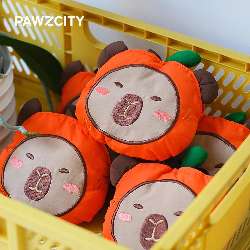 A yellow crate filled with multiple plush PAWZCITY Capybara waste bag dispensers, featuring an adorable design of a capybara face inside an orange fruit costume.