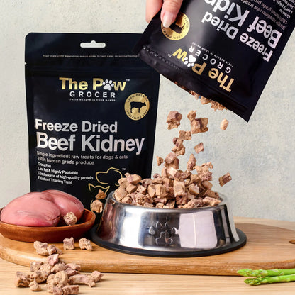 A hand pouring 100% pure freeze-dried beef kidney treats from the pouch into a silver pet bowl, showcasing the raw, vitamin-packed cubed texture that acts as nature&