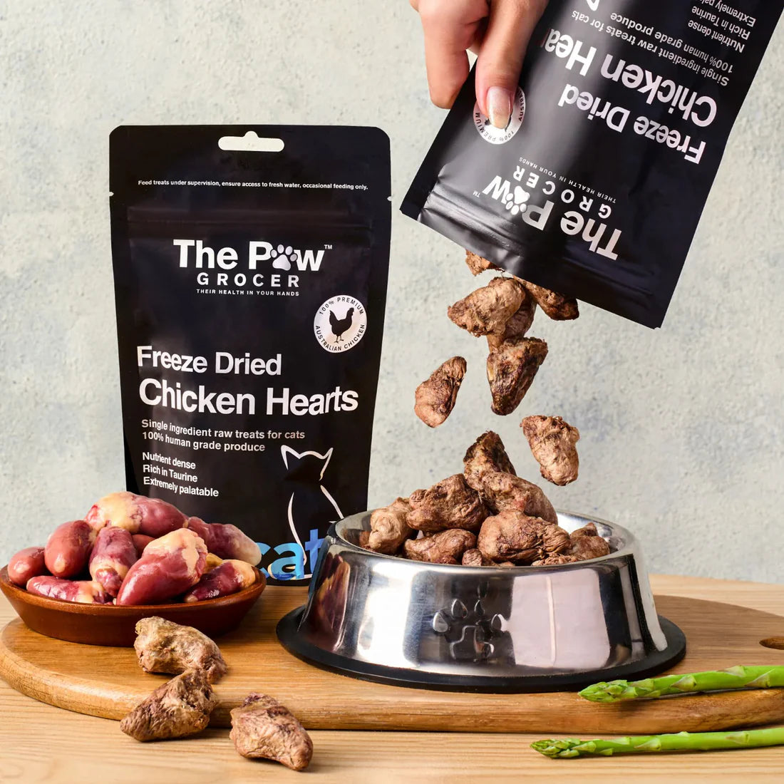 A hand pouring 100% Australian freeze-dried chicken hearts into a pet bowl, showing the raw, crunchy cubed texture that acts as a natural multivitamin for felines.