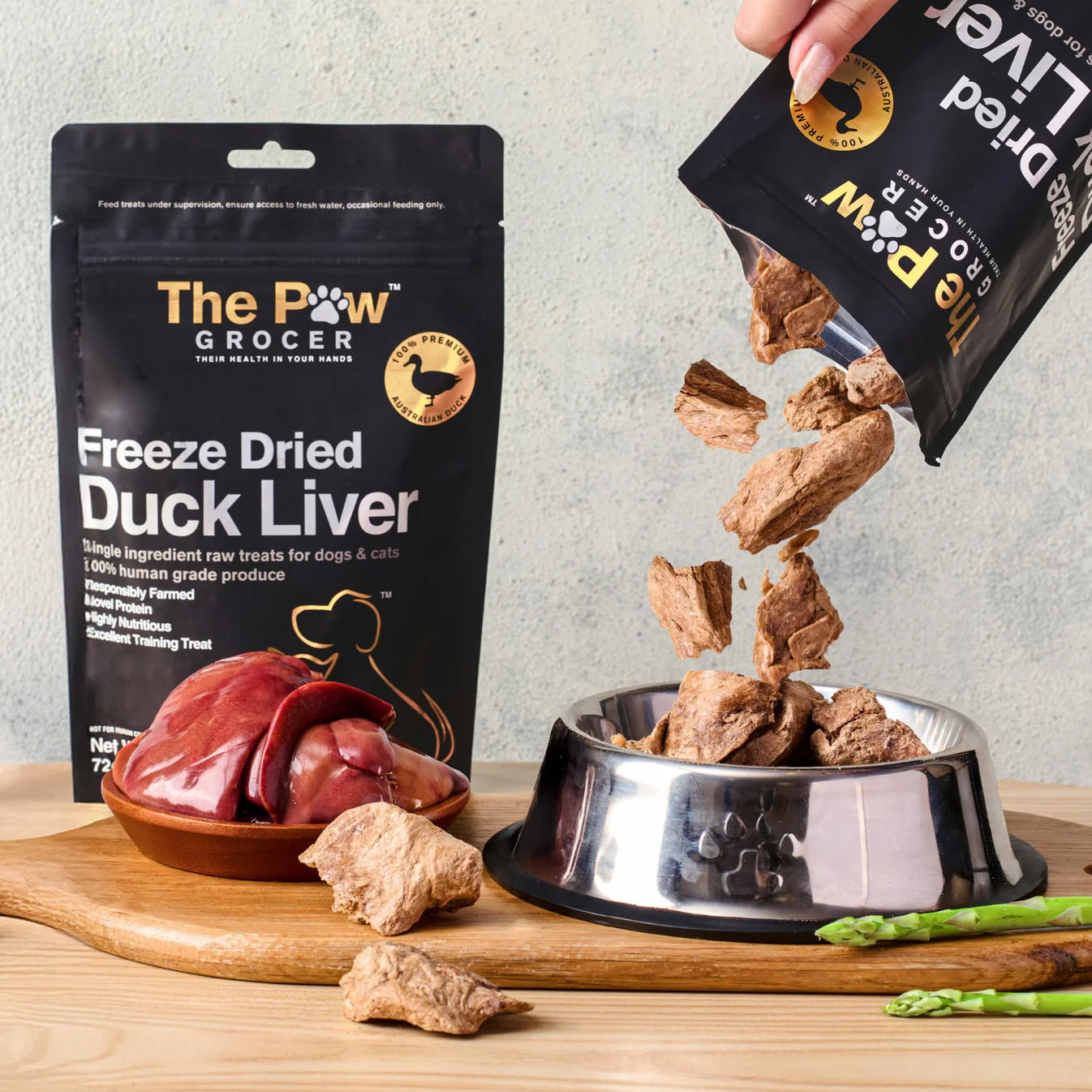 A hand pouring 100% pure freeze-dried duck liver treats from the pouch into a silver pet bowl, showcasing the highly nutritious, raw cubed texture that serves as nature&