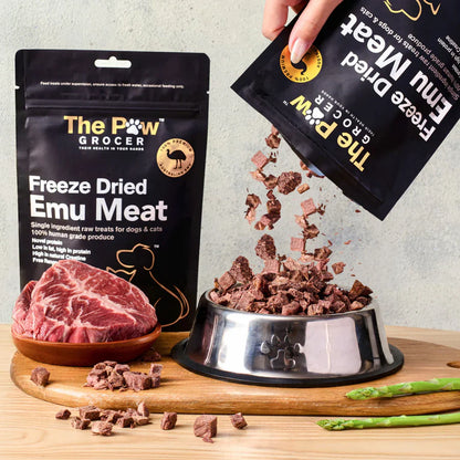 A hand pouring 100% pure freeze-dried emu meat treats from the pouch into a silver pet bowl, showcasing the highly digestible, raw cubed texture that is perfect for sensitive stomachs.