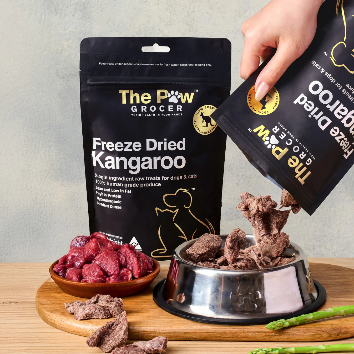 A hand pouring 100% pure Australian freeze-dried kangaroo treats from the pouch into a silver pet bowl, showcasing the natural, raw cubed texture that picky eaters love.