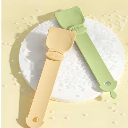 Two minimalist cat liquid treat spoons in soft green and pastel orange resting on a textured white surface, highlighting the durable, food-safe HIPS material.