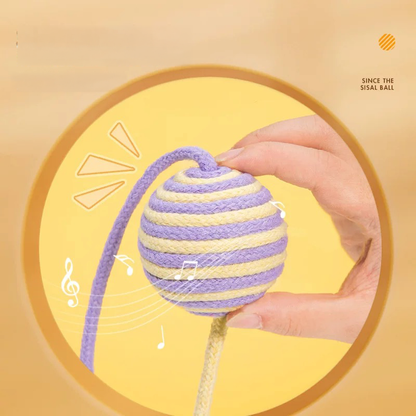 A hand holding a purple and yellow striped sisal cat toy ball with illustrated music notes around it, highlighting the gentle built-in rattle sound.