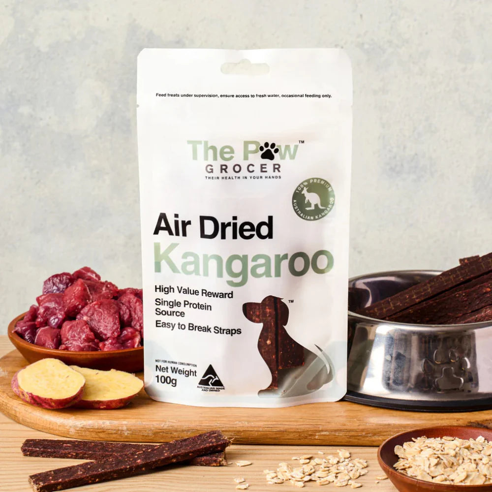 Detailed showcase of The Paw Grocer Kangaroo packaging on a wooden board. Surrounded by raw kangaroo meat, sweet potato slices, and oats to highlight natural ingredients.