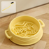 A Rock Yellow silicone slow feeder bowl placed on a wooden floor, with a graphic of a cleaning brush in the top left corner highlighting effortless maintenance.
