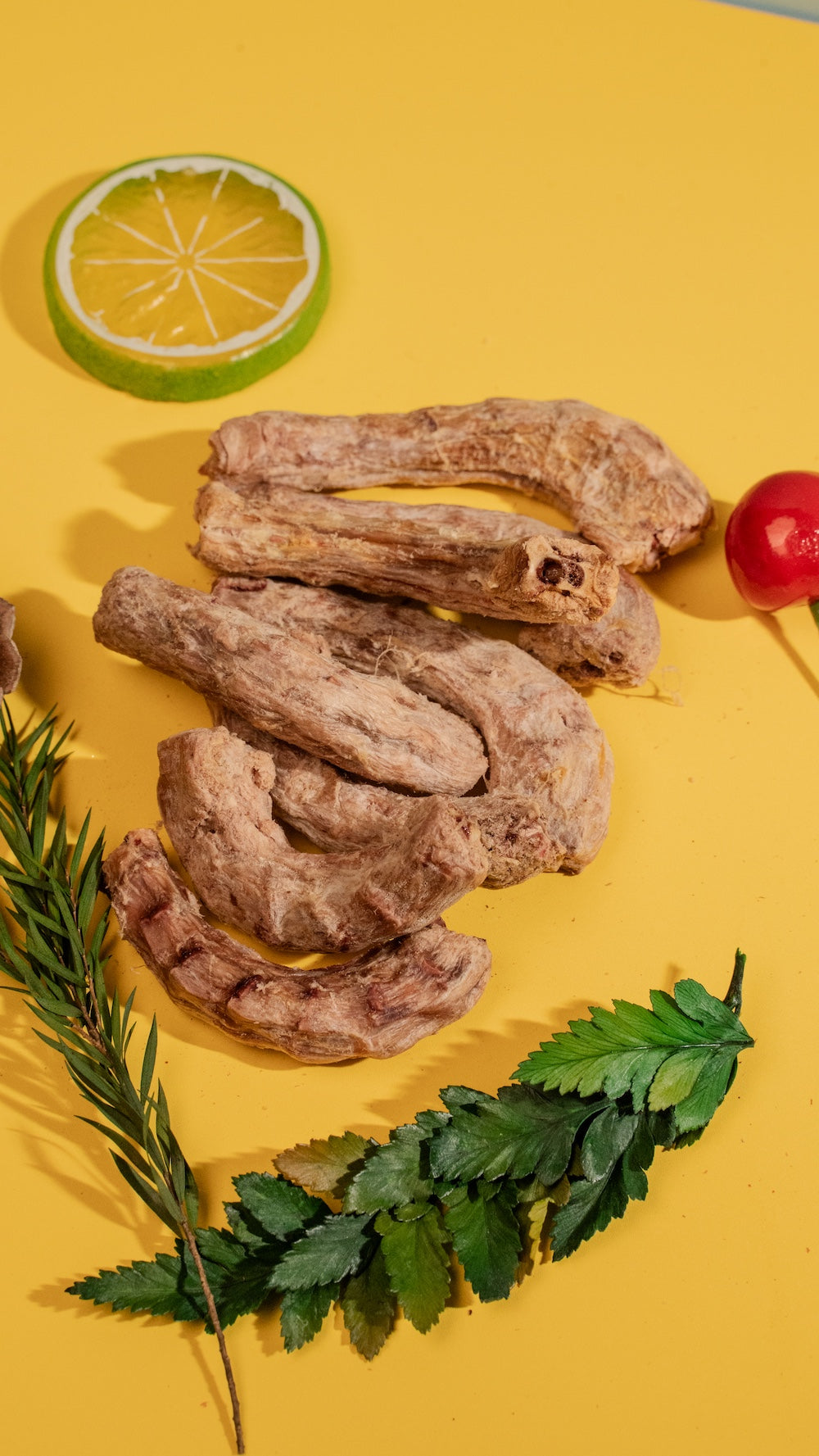 Freeze-dried chicken neck pet treats beautifully arranged on a vibrant yellow background with green leaves and a lemon slice, illustrating a healthy and 100 percent natural snack.