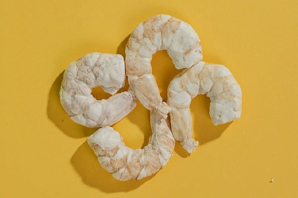 Three freeze-dried whole shrimp treats arranged artistically on a vibrant yellow background, highlighting the high-protein and low-fat ocean delicacy for cats and dogs.