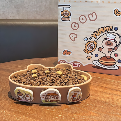 slow feeder and pet food next to a cartoon-themed box on a wooden surface