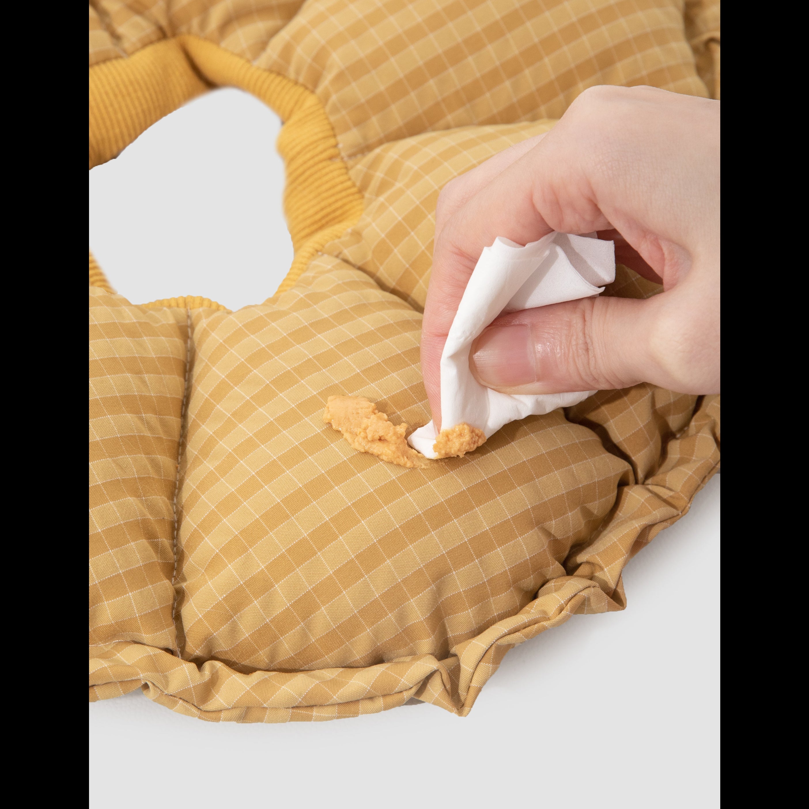 A hand using a white tissue to effortlessly wipe away a smudge of wet pet food from the stain-resistant yellow gingham collar.