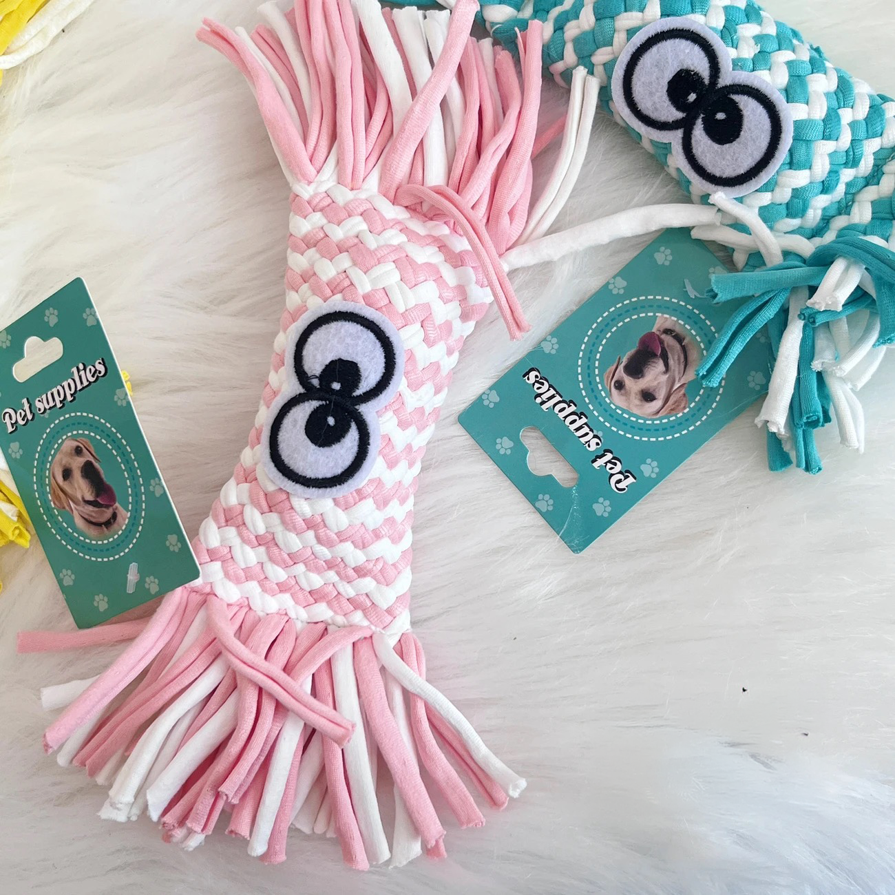 The bright strawberry pink variant of the Woven Candy Squeaky Toy. The close-up shows the wrapped candy shape, the thick braided fabric texture, and the large cartoon eyes.