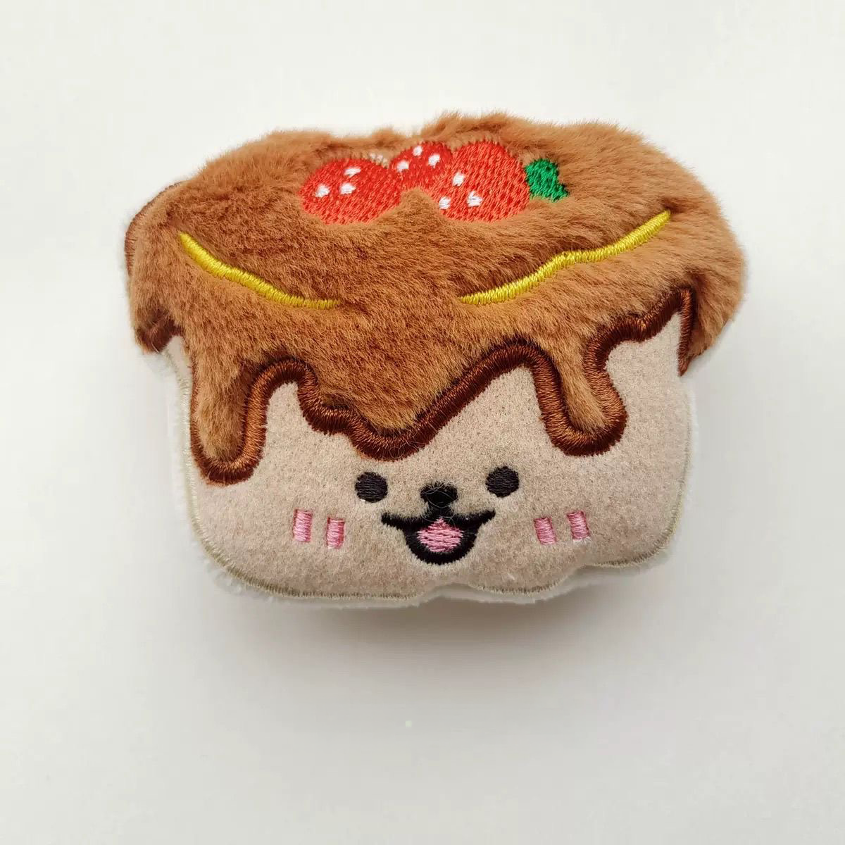 A soft strawberry pudding cake plush toy featuring a chocolate drizzle design and two embroidered strawberries.