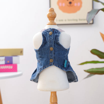 Front view of the denim dog dress on a mannequin, showcasing the three classic bronze-tone snap buttons and pastel pink stretchy shoulder straps.