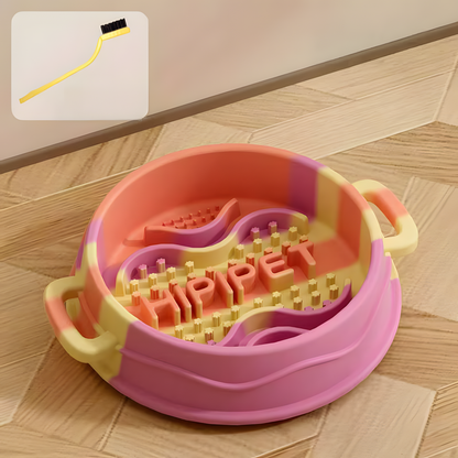 A Sunny Orange pastel swirl silicone slow feeder bowl on a wooden floor, featuring an inset graphic of the complimentary cleaning brush used to wash the deep maze dividers.