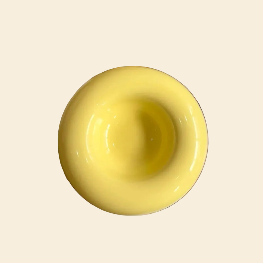 Top-down view of a Sunshine Yellow ceramic bagel pet bowl resting on an art book, showcasing its perfectly circular 80ml center capacity and vibrant glossy finish.