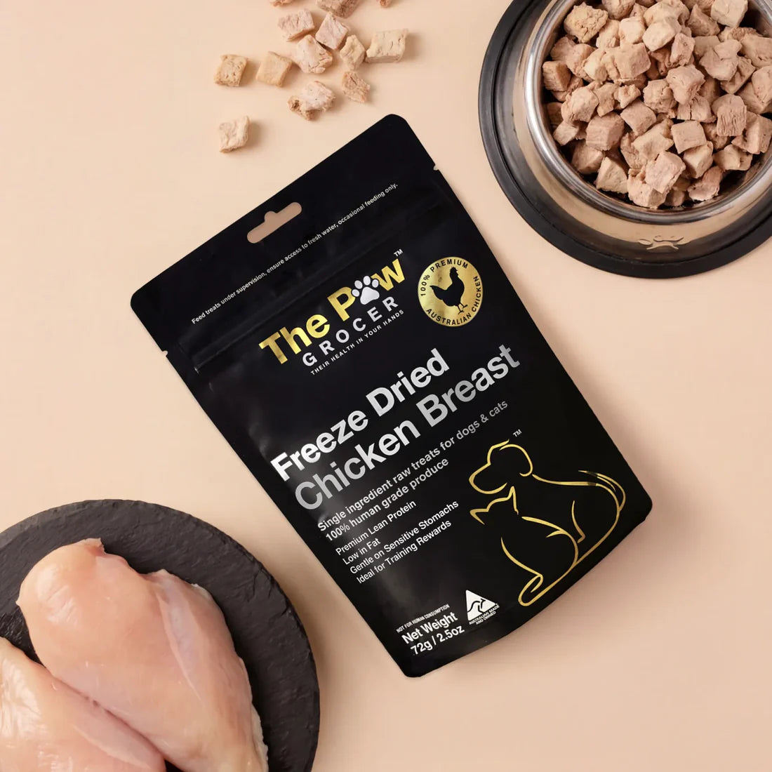 A top-down view of The Paw Grocer Freeze-Dried Chicken Breast pouch surrounded by fresh raw chicken breast and a silver bowl filled with the low-fat, cubed everyday training treats.