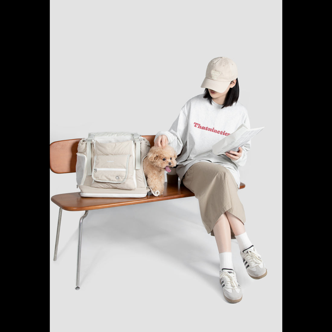 A pet parent sitting on a bench reading, with her small dog resting securely in the LéJoyee open-top front pet carrier backpack.