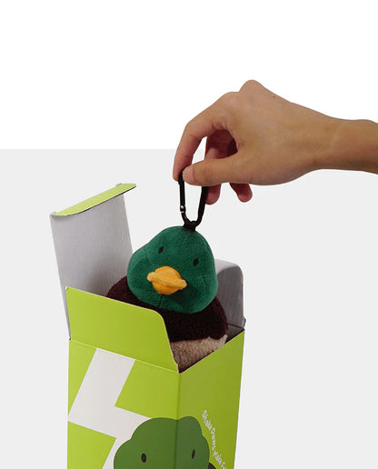 A hand lifting the PAWZCITY plush duck out of its green packaging box by its sturdy black carabiner clip, showcasing the unboxing experience.