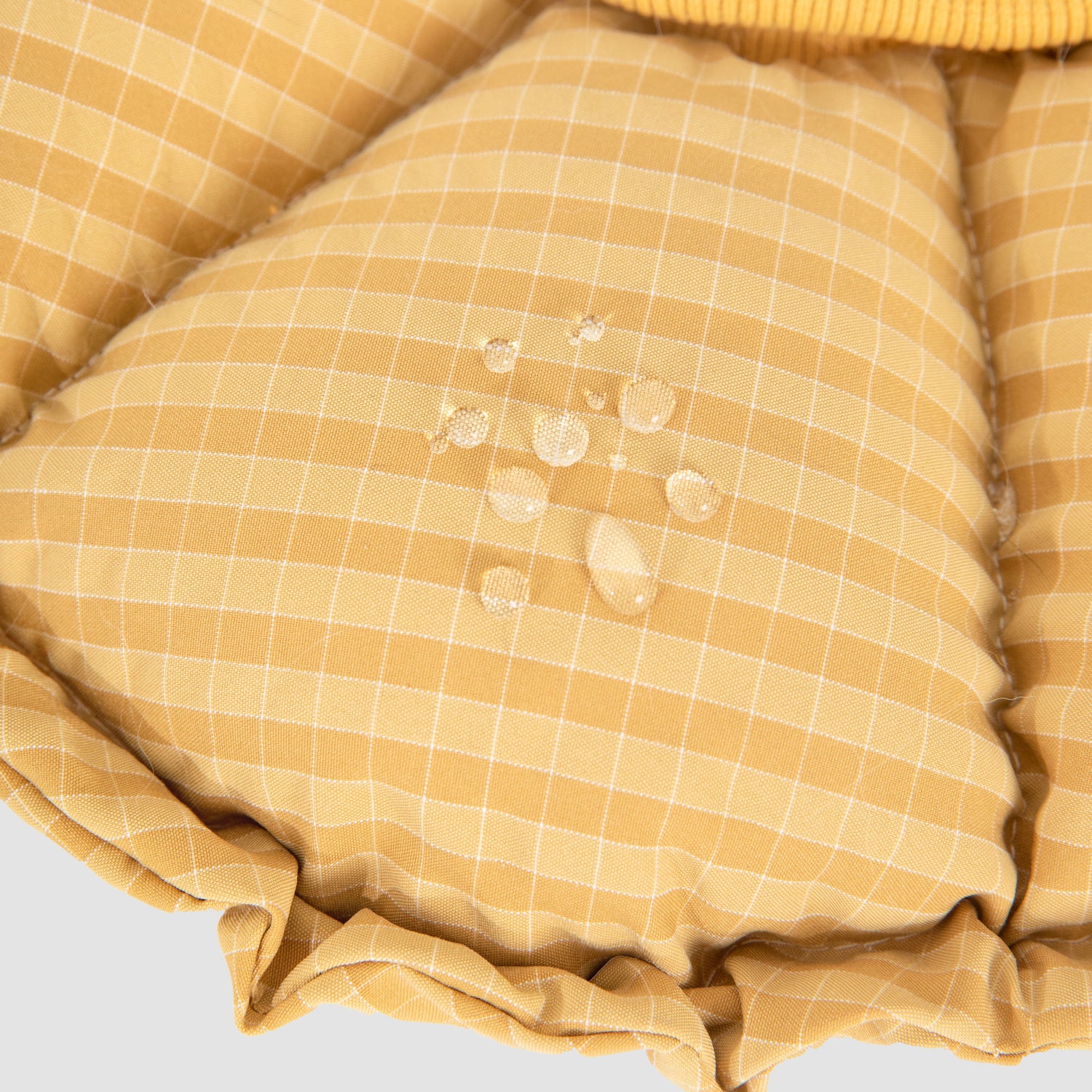 Macro shot showing water droplets seamlessly beading up on the water-repellent yellow gingham fabric of the HiDREAM soft recovery collar.