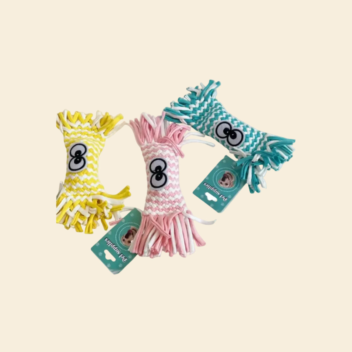 Three tightly braided woven candy-shaped dog toys in yellow, pink, and teal blue, lying on a yellow background. Each features large cartoon eyes and "Pet supplies" tags.
