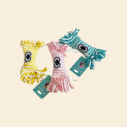 Three tightly braided woven candy-shaped dog toys in yellow, pink, and teal blue, lying on a yellow background. Each features large cartoon eyes and "Pet supplies" tags.