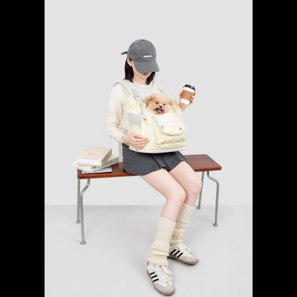 A pet owner sitting with a coffee cup, keeping her small dog cozy and secure in the pale yellow, anti-sag front carrier backpack.