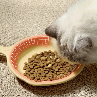 A fluffy white cat eating kibble from the yellow Mango Little Skillet plate. A red graphic grid highlights the expertly rounded inner walls that make food glide to the center.